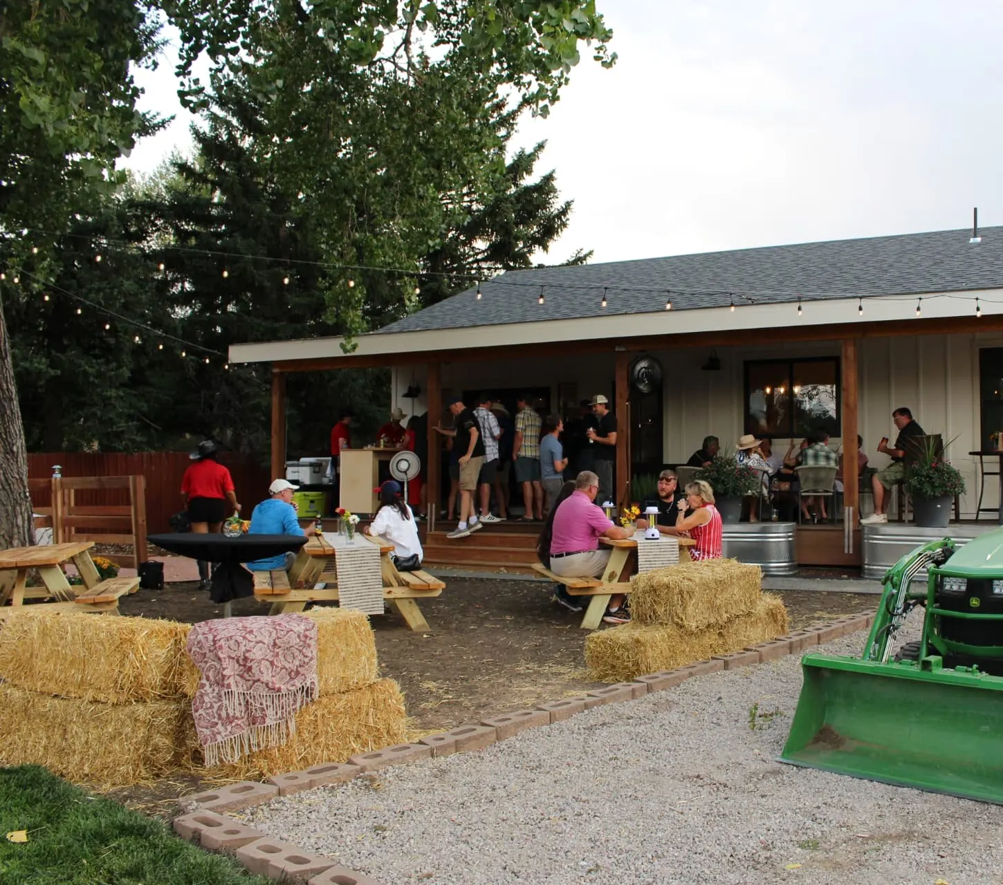 Guests seated at picnic tables and hay bales under string lights at a Bear n Bull outdoor event.