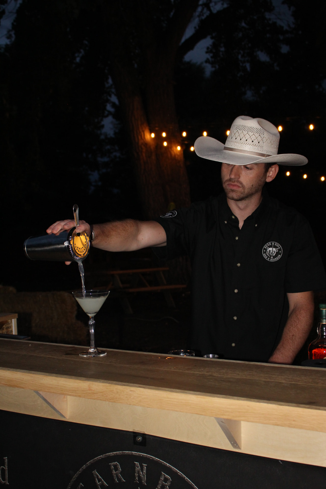 Bear n Bull bartender in a cowboy hat pouring a cocktail into a coupe glass at the bar.