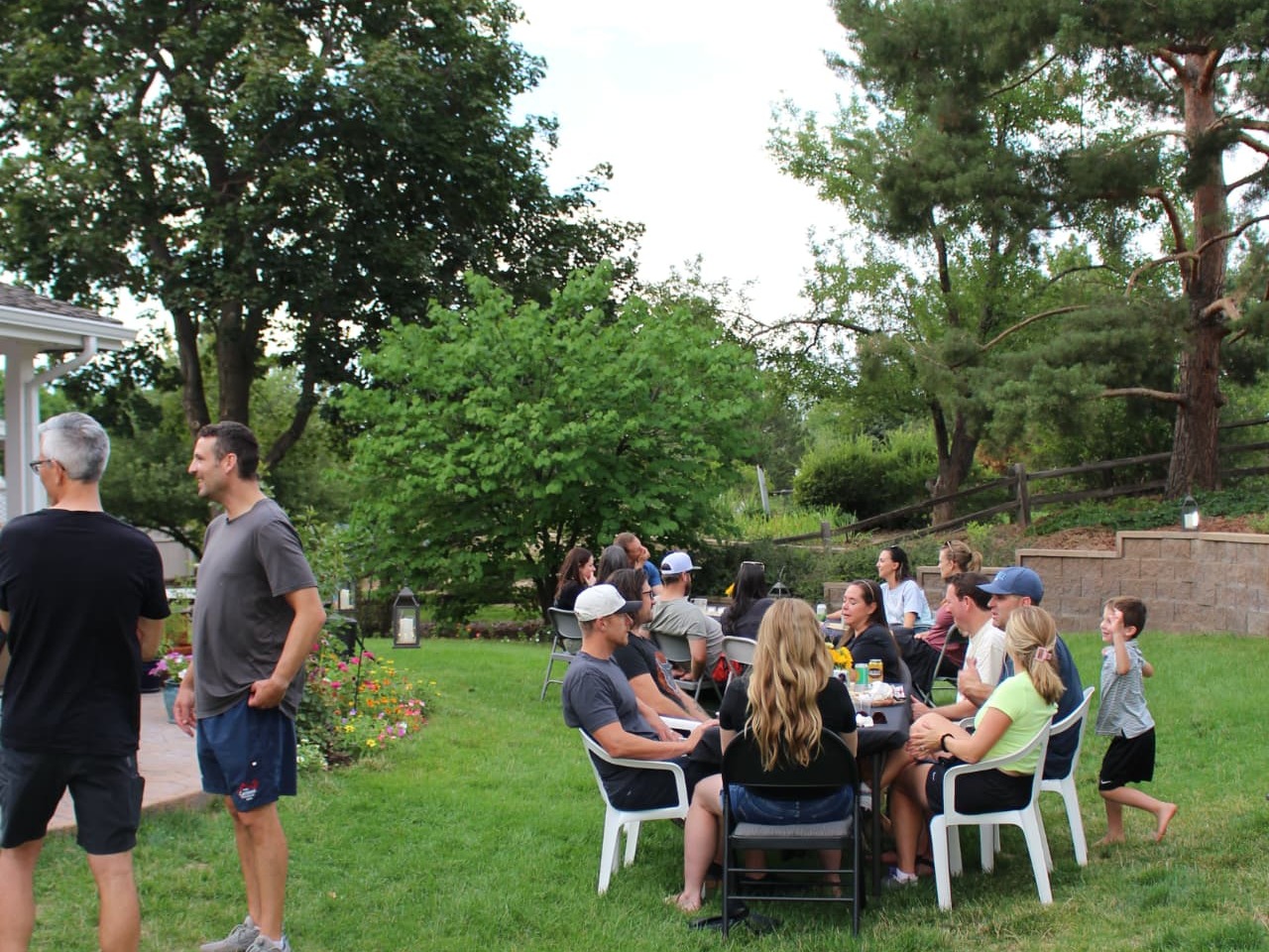 Guests gathered at a backyard party with a child playing on the lawn.