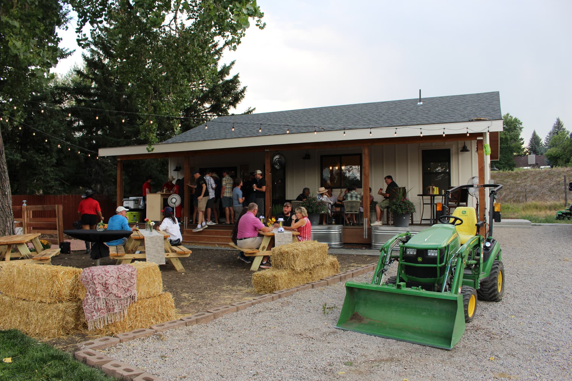 Outdoor Bear n Bull ranch dinner with guests, hay bales, and a tractor.