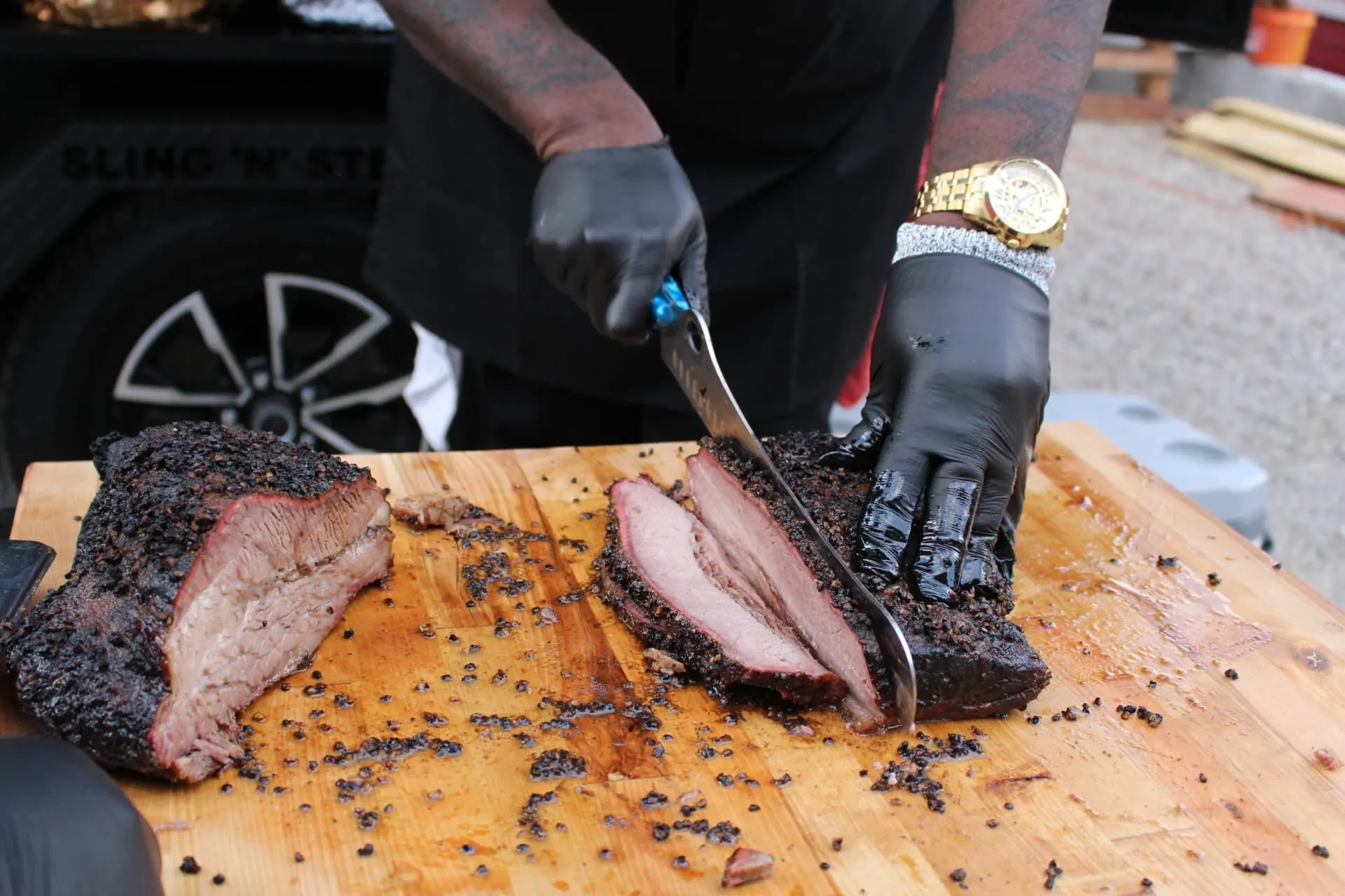 Bear n Bull pitmaster slicing a smoked brisket on a wooden board beside the trailer.