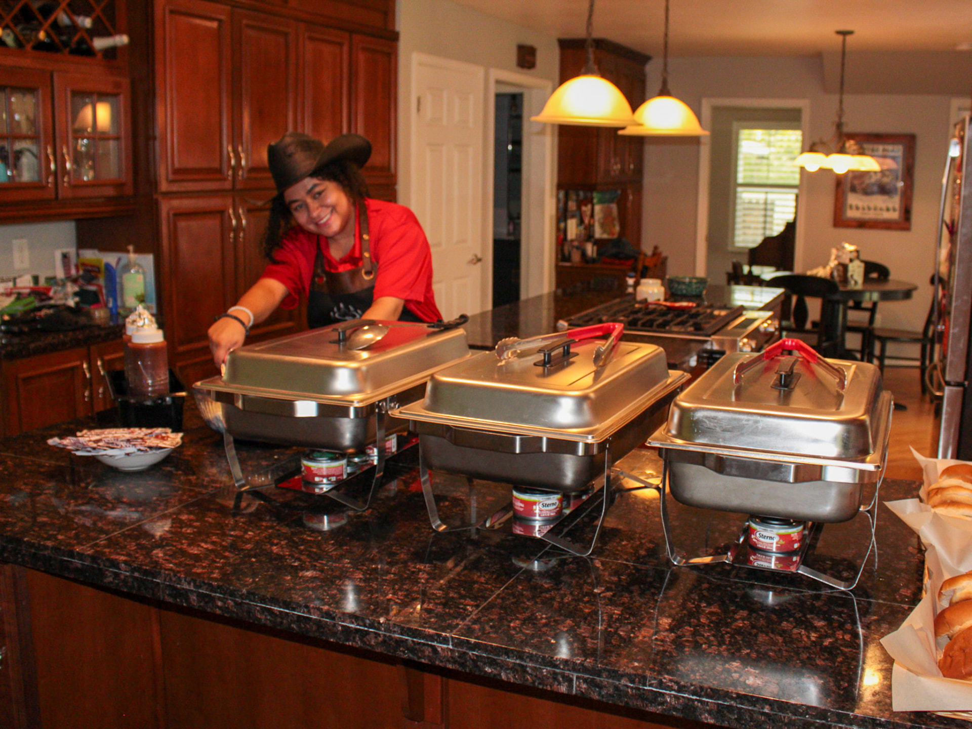 Bear n Bull team member in a red shirt and cowboy hat serving smoked meats from chafing trays at a buffet line.