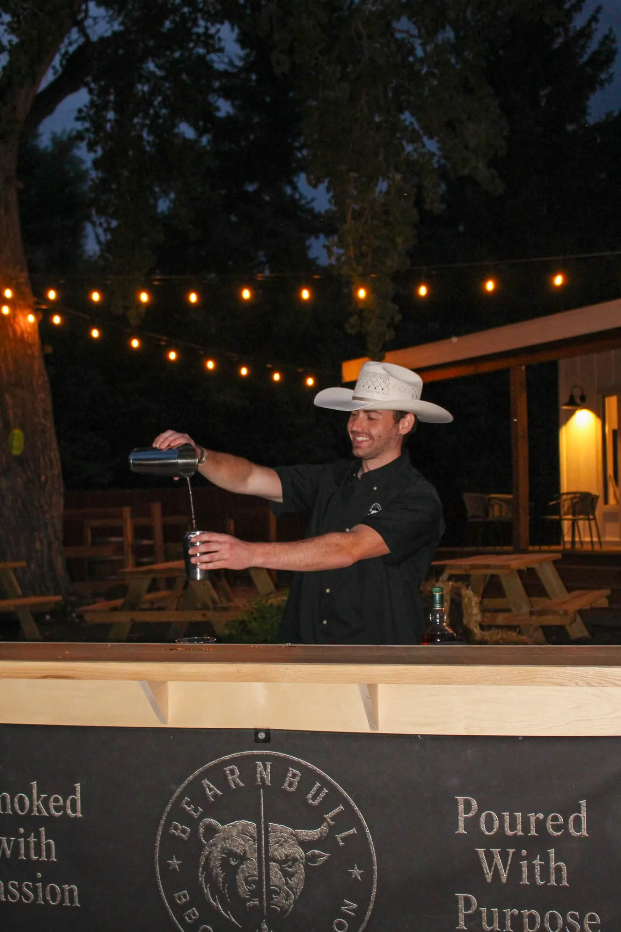 Bear n Bull bartender mixing a cocktail at the branded outdoor bar under string lights.